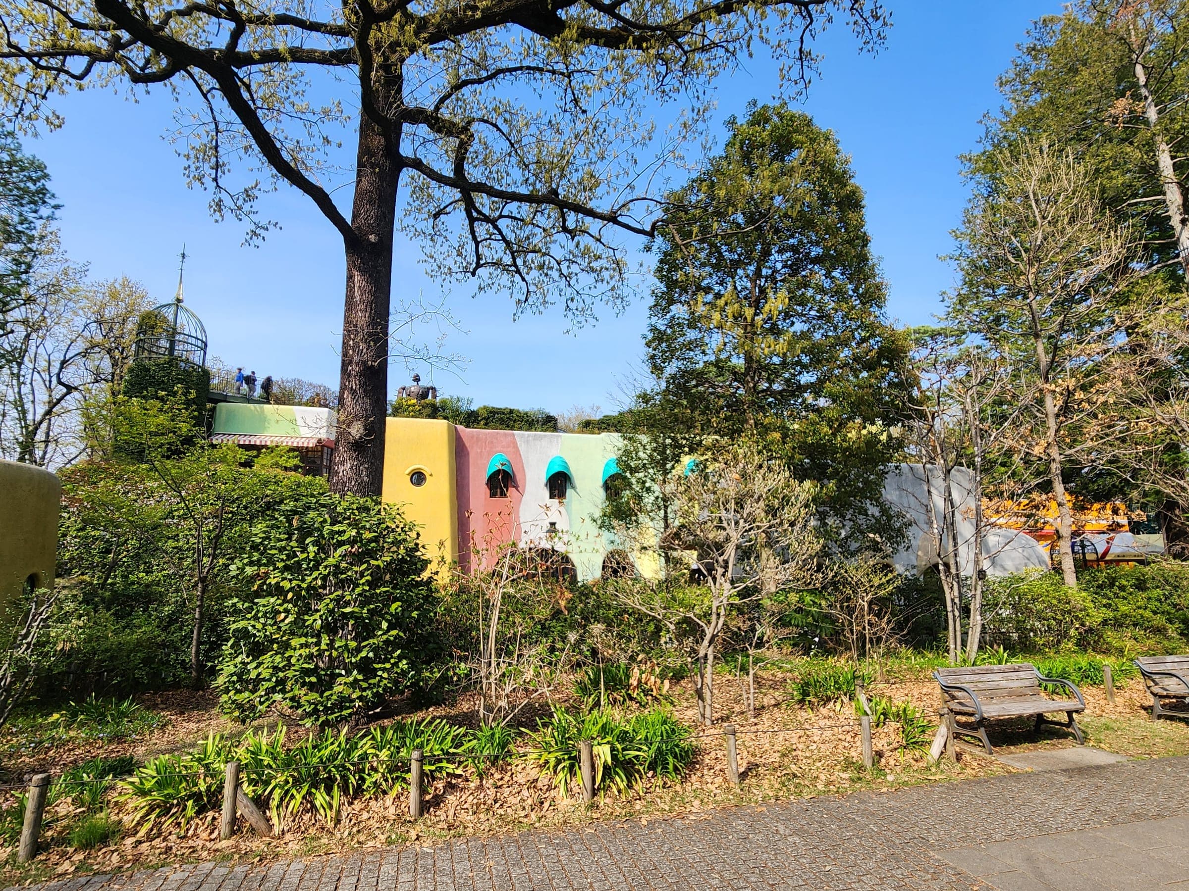 The museum's pastel façade, yellow, coral and mint, seen through the trees of Inokashira Park